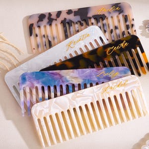 May include: A collection of personalized combs in various colors and patterns. The combs feature names in gold script. Colors include white, black, brown, blue, and purple. The combs are arranged on a light-colored surface.