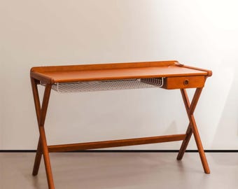 May include: A mid-century modern wooden desk with a warm brown finish. The desk features a rectangular tabletop, a small drawer, and a wire mesh shelf. The legs are crossed for stability. A stylish and functional piece for any workspace.