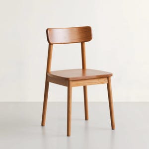 May include: A wooden chair with a light brown finish. The chair has a rectangular seat, four straight legs, and a small backrest. The design is simple and modern, suitable for dining or as an accent piece.