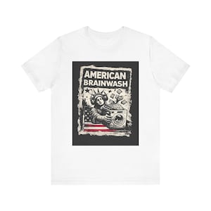 May include: White t-shirt featuring a graphic with the text "AMERICAN BRAINWASH". The graphic depicts the Statue of Liberty with a washing machine, money, and the American flag. The design is in black and white.