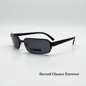 May include: Black rectangular sunglasses with dark gray lenses. The frames are black metal with a subtle rectangular shape. The brand name "BCBGMAXAZRIA" is visible on the lower left lens. The text "Second Chance Eyewear" is at the bottom.