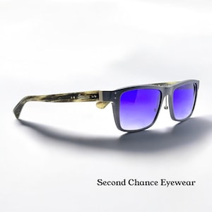 May include: Square-framed sunglasses with a dark grey frame and gradient blue lenses. The temples are a light brown with a wood grain pattern. The text "Second Chance Eyewear" is below the sunglasses.