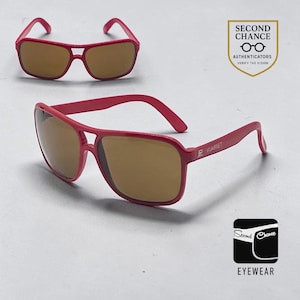 May include: Bright pink sunglasses with brown lenses and a double bridge frame. The temple arm features the Vuarnet logo. The image includes a Second Chance Authenticators shield logo and a Second Chance Eyewear logo with the text Verify the Vision.