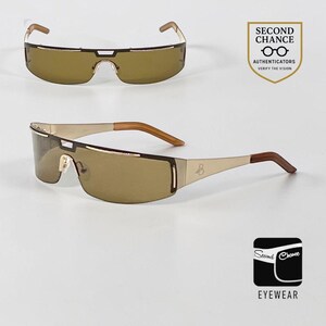 Puede incluir: Gafas de sol tipo máscara con una lente marrón continua y una montura de metal en tono dorado. Las varillas son doradas con puntas marrones y un pequeño logotipo es visible en el lateral. Incluye el logotipo de Second Chance Authenticators.