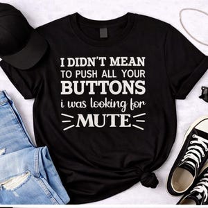 Peut inclure: T-shirt noir avec le texte blanc "I DIDN'T MEAN TO PUSH ALL YOUR BUTTONS i was looking for MUTE". Le t-shirt est présenté avec un jean bleu, une casquette noire, des lunettes de soleil et des baskets noires et blanches.
