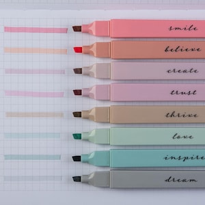 May include: A collection of eight pastel-colored highlighters with matching ink swatches on graph paper. Each highlighter has a different color and the words "smile", "believe", "create", "trust", "thrive", "love", "inspire", and "dream" are printed on the side.