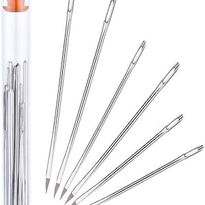 May include: A collection of sewing needles, some arranged in a fan shape, with a clear plastic tube with an orange cap. The needles are silver and have a sharp point and an eye for threading.