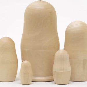 May include: A set of five unfinished wooden nesting dolls, also known as Matryoshka dolls, in varying sizes. The dolls are light brown and have a smooth, unpainted surface, ready for customization. The largest doll is approximately 7 inches tall.