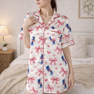 May include: White satin sleep shirt with a red trim, short sleeves, and a button-down front. The shirt is patterned with pink bows, hearts, and blue cylindrical graphics. The sleep shirt is knee-length.