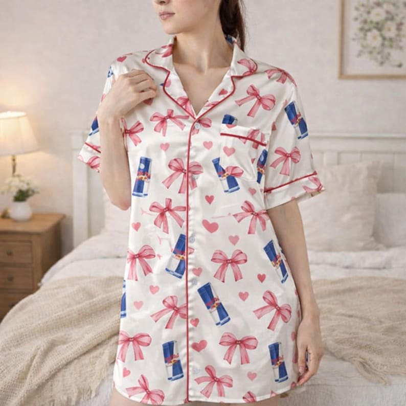May include: White satin sleep shirt with a red trim, short sleeves, and a button-down front. The shirt is patterned with pink bows, hearts, and blue cylindrical graphics. The sleep shirt is knee-length.