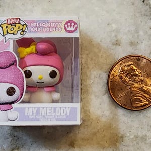 Puede incluir: Figura de My Melody de Hello Kitty and Friends en una vitrina de pl&aacute;stico transparente. La figura es rosa y blanca con un lazo amarillo. Una moneda est&aacute; al lado de la figura para la comparaci&oacute;n de tama&ntilde;o.