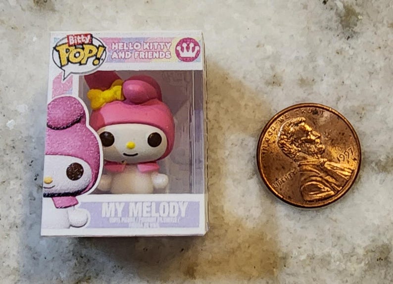 Puede incluir: Figura de My Melody de Hello Kitty and Friends en una vitrina de pl&aacute;stico transparente. La figura es rosa y blanca con un lazo amarillo. Una moneda est&aacute; al lado de la figura para la comparaci&oacute;n de tama&ntilde;o.