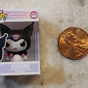 Puede incluir: Una figura de Bitty Pop! de Kuromi de Hello Kitty and Friends, en una vitrina de pl&aacute;stico transparente. La figura es negra, blanca y rosa. Una moneda de un centavo estadounidense est&aacute; al lado de la figura.