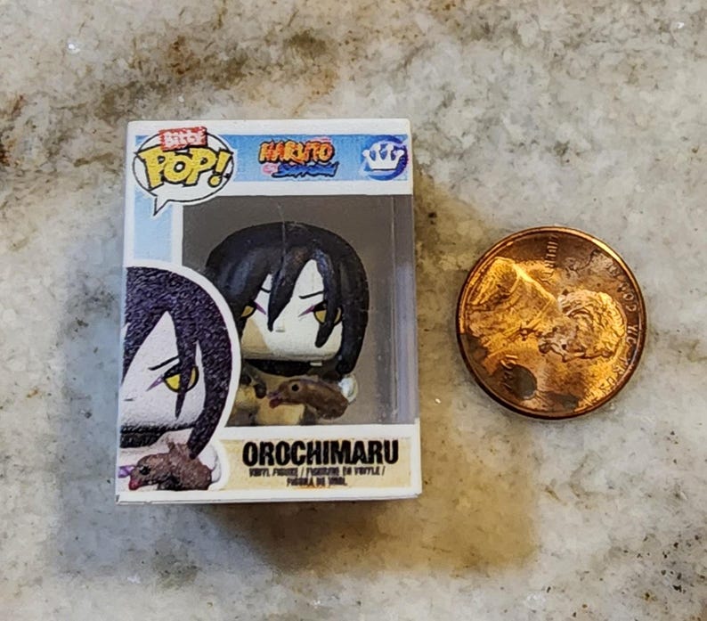 May include: A miniature Orochimaru vinyl figure from the Naruto anime series, displayed in its original box. The figure has black hair and yellow eyes. A penny is next to the figure for size comparison. The box reads "Bitty Pop!" and "Orochimaru".