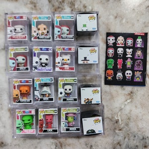 May include: A collection of 13 Nightmare Before Christmas Funko Pop! figures in clear plastic boxes. The figures include Jack Skellington, Sally, Zero, Oogie Boogie, and more. The boxes are arranged in three rows of four boxes each. The figures are all in their original packaging. The boxes are labeled with the character's name and the Funko Pop! logo.