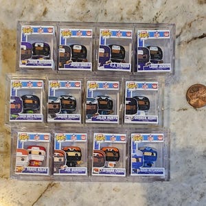 May include: A collection of twelve miniature Funko Pop NFL figures housed in clear plastic display cases, arranged in three rows. Each box features a specific player name and team colors. A copper penny is placed to the right for scale reference.