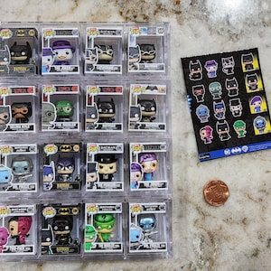 May include: A collection of 18 Batman Funko Pop figures in clear plastic display cases. The figures are arranged in three rows of six. Each figure is a different character from the Batman universe, including Batman, Robin, Catwoman, The Joker, The Riddler, and Two-Face. The figures are all in their original packaging.