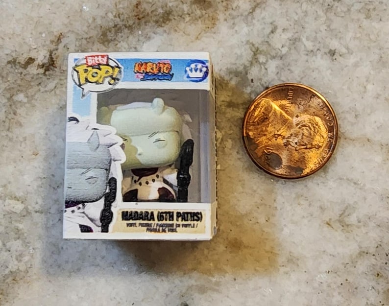 May include: A small, boxed "Bitty Pop!" figure of Madara (6th Paths) from the Naruto series. The figure is in a clear plastic case next to a US penny. The box is white with blue and yellow accents. The figure is primarily green, white, and black.