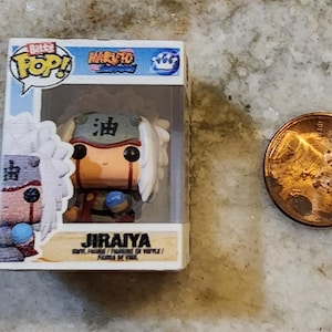 May include: A miniature Jiraiya vinyl figure from the Naruto anime series, displayed in a clear plastic box. The figure has white hair, a green headband, and a brown outfit. A penny is next to the figure for size comparison.