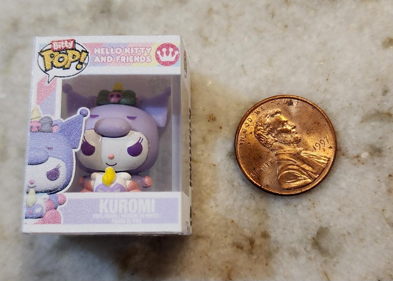 Puede incluir: Una figura Bitty Pop! Hello Kitty and Friends de Kuromi en una vitrina de pl&aacute;stico transparente. La figura es morada, blanca y amarilla. Una moneda est&aacute; al lado de la figura para comparar el tama&ntilde;o.