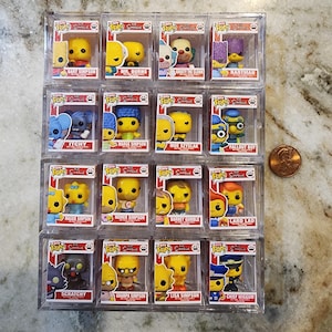 May include: A collection of Funko Pop! figures featuring characters from The Simpsons animated television series. Each figure is in a clear plastic display case. Characters include Bart Simpson, Homer Simpson, and Marge Simpson.