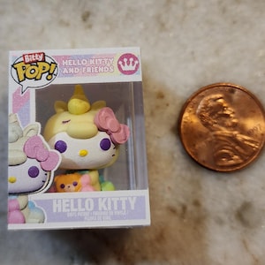 Puede incluir: Una figura de Bitty Pop! Hello Kitty and Friends en una vitrina de pl&aacute;stico transparente. La figura es un Hello Kitty unicornio amarillo con un lazo rosa. Una moneda de un centavo est&aacute; al lado de la figura para comparar el tama&ntilde;o. La caja dice "Hello Kitty" y "Bitty Pop!"