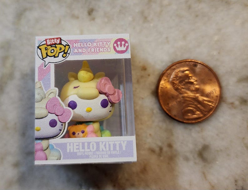 Puede incluir: Una figura de Bitty Pop! Hello Kitty and Friends en una vitrina de pl&aacute;stico transparente. La figura es un Hello Kitty unicornio amarillo con un lazo rosa. Una moneda de un centavo est&aacute; al lado de la figura para comparar el tama&ntilde;o. La caja dice "Hello Kitty" y "Bitty Pop!"