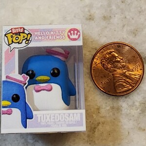 Puede incluir: Una figura de Bitty Pop! de Tuxedosam de Hello Kitty and Friends. La figura del ping&uuml;ino azul lleva una pajarita y un sombrero rosas. La figura est&aacute; en una vitrina de pl&aacute;stico transparente junto a una moneda.