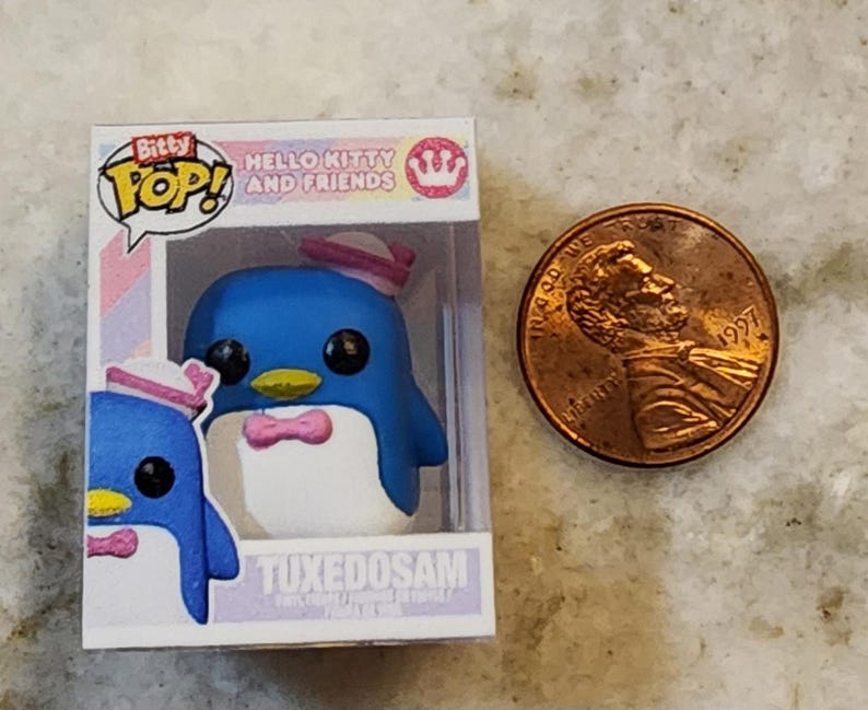 Puede incluir: Una figura de Bitty Pop! de Tuxedosam de Hello Kitty and Friends. La figura del ping&uuml;ino azul lleva una pajarita y un sombrero rosas. La figura est&aacute; en una vitrina de pl&aacute;stico transparente junto a una moneda.