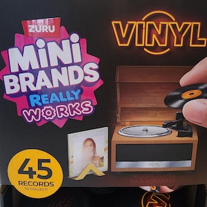 May include: A Zuru Mini Brands Really Works product box featuring a miniature wooden-style record player and a small album cover. The packaging displays the text Vinyl, 45 Records to Collect, and Record Player Sold Separately on a black background.