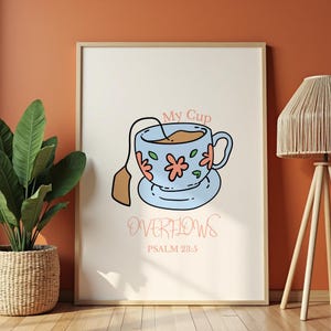 Może przedstawiać: Oprawiony wydruk przedstawiający niebieski kubek z różowymi kwiatowymi akcentami i torebką herbaty. Słowa "My Cup Overflows" i "Psalm 23:5" są napisane w miękkim, brzoskwiniowo-różowym kolorze. Grafika jest na kremowym tle.