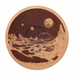 May include: A brown cork coaster with a detailed etched illustration of a futuristic lunar landscape. The design features planets, domed structures, and a vehicle, set against a starry sky. The coaster is round.