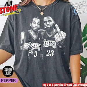 May include: A charcoal gray short-sleeve t-shirt featuring a black and white graphic of two basketball players in Sixers jerseys with the numbers 3 and 23. One player holds a bottle and the other holds a cigarette while gesturing with a finger.