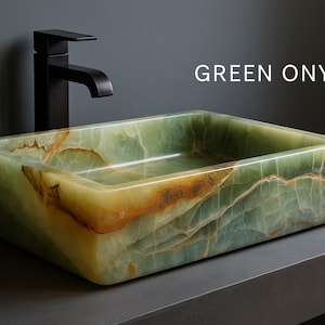 May include: A rectangular green onyx sink with a black faucet. The sink has a natural, veined pattern with shades of green, brown, and yellow. The text "GREEN ONYX" is displayed on the image. This sink is a bathroom fixture.
