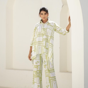 May include: A two-piece matching set comprising a button-down shirt and wide-leg trousers. The set is white with a light green geometric pattern. The shirt has long sleeves and a collared neckline. The trousers have a high waist and a relaxed fit.