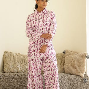 May include: A white two-piece pajama set featuring a repeating magenta seahorse design. The set comprises a button-down shirt and wide-leg trousers. The model is wearing the pajama set.