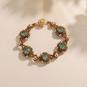 May include: A beaded bracelet featuring iridescent teal-colored stones and small, round, bronze-colored beads. The bracelet has a gold-colored clasp and is displayed on a neutral background. The bracelet's design incorporates floral-like patterns.