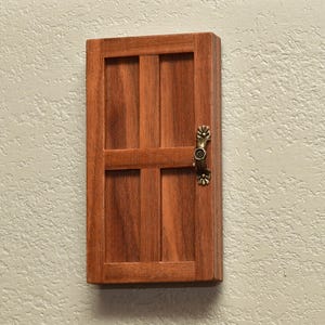 May include: A rectangular wooden door with a medium brown finish and a visible wood grain pattern. The door features a four-panel design divided by a central vertical and horizontal rail. An ornate, antique brass-colored metal handle is attached.