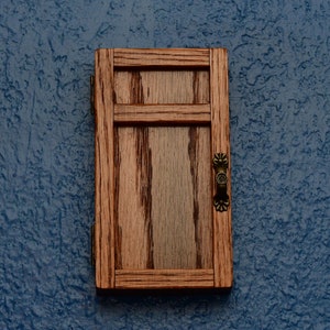 May include: A small wooden door with a brown stain and a brass handle. The door is closed and has a simple design with two horizontal panels.