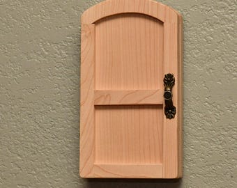 以下が含まれることがあります： 木目がはっきりと見える明るい色の天然木で作られた、小さなアーチ型の木製ドア。ドアには水平の横木があり、ドアフレームの右側にはアンティーク調の真鍮色の金属製ハンドルが取り付けられています。