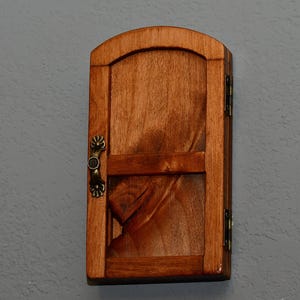 May include: A small wooden door with a decorative metal handle. The door is closed and has a dark brown stain.
