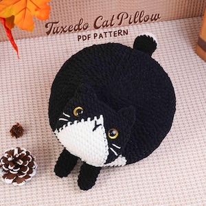 May include: A handmade black and white Tuxedo Cat Pillow. The round pillow features a cat face with yellow eyes, white markings, and a small tail. The text "Tuxedo Cat Pillow PDF PATTERN" is visible in the image.
