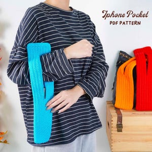 May include: A person holding a turquoise blue crochet iPhone pocket. The image also shows orange and red crochet pockets, and the text "iPhone Pocket PDF PATTERN". The pockets are displayed on a wooden trunk.