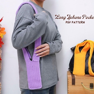 Könnte beinhalten: Eine Person präsentiert eine handgefertigte, lavendelfarbene Häkeltasche für das Telefon mit einem langen Riemen. Der Text "Long Iphone Pocket PDF Pattern" wird angezeigt. Eine orangefarbene Häkeltasche für das Telefon und eine schwarze Tasche befinden sich auf einer Holzkiste.