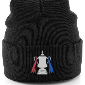 Op de afbeelding: Zwarte gebreide beanie met een zilveren trofee-embleem en rode en blauwe linten. De hoed is gemaakt van geribbelde gebreide stof, een klassiek en veelzijdig accessoire.