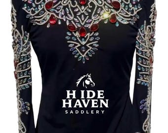 May include: Black equestrian show shirt with long sleeves. The shirt features elaborate embellishments of clear and red gemstones and pearls around the collar, shoulders, and sleeves. The brand "HIDE HAVEN SADDLERY" is printed on the front.