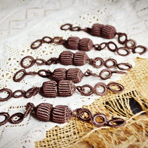 May include: A set of six brown tassel tiebacks with metal rings. The tiebacks are made of a soft, woven fabric and have a classic design.