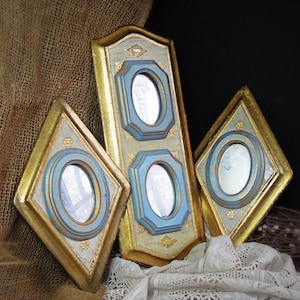 May include: A set of three wall mirrors with gold-toned frames and light blue oval accents. The central rectangular mirror features two oval glass panels, while the two flanking diamond-shaped mirrors each contain a single oval glass panel.