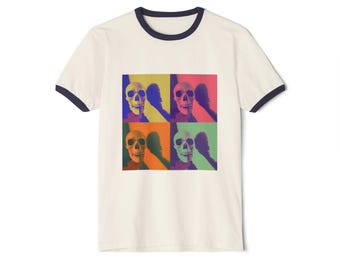 May include: Cream-colored ringer t-shirt with a navy blue trim. The shirt features a pop art style design of a skull in four different color blocks: yellow, red, orange, and green. The skull's shadow is visible in each block.