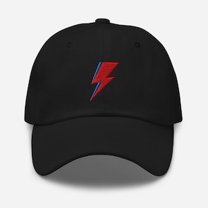 May include: Black baseball cap with a red and blue embroidered lightning bolt design. The cap has a curved brim and an adjustable strap at the back. A stylish accessory for casual wear.